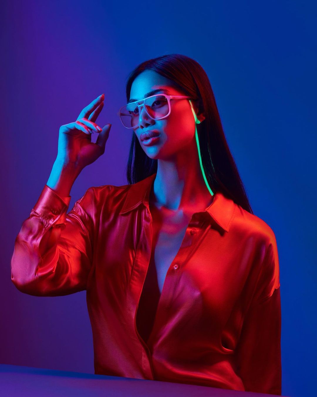 Glamour shot of an Asian woman wearing glasses and a red shirt, posing in a studio with blue and purple lighting. Beauty and fashion.